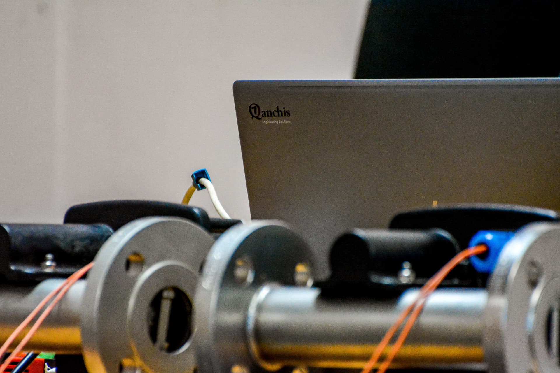 Qanchis laptop above a flanged flow-meter test rig in the workshop