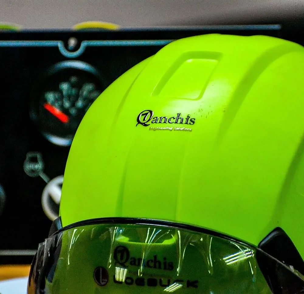 Qanchis-branded safety helmet in front of a control panel
